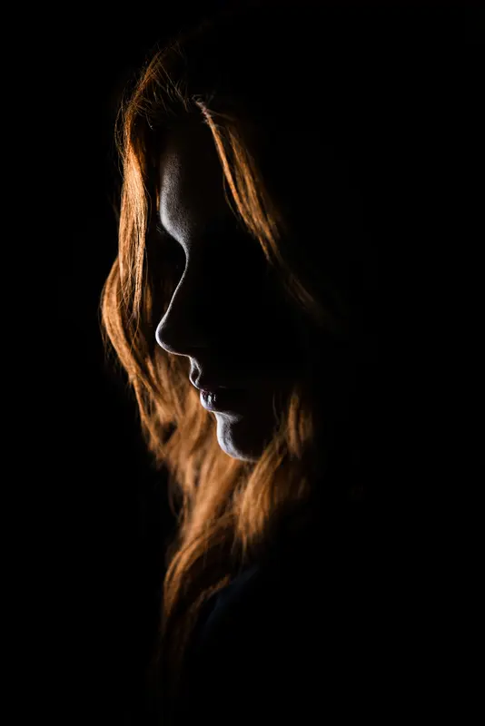 Profil einer Frau mit kupferrotem Haar im Halbdunkel
